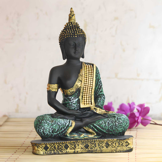 Decorative Buddha statue with green and gold details on a wooden surface with purple flowers in the background.